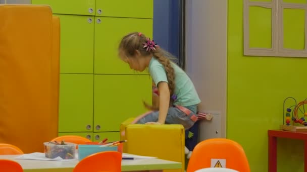 Niño sube a un montón de almohadas caminando por la habitación Niña rubia está jugando con almohadas en forma de cubo amarillo jugando a las sillas naranjas de la sala en los escritorios — Vídeo de stock