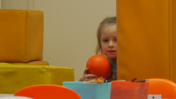 Dítě drží oranžové hračky sedí schovává mezi polštáře blond holčička je Playing With Yellow Cube-Shaped polštáře hraje místnosti oranžová židle — Stock video