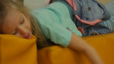 Lying Yellow Cube-Shaped yastık alır üzerinde küçük sarışın kız mavi tişört kalın kaplama ile oynarken odasında oynuyor bir yastık üzerinde oturan çocuktur