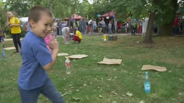 Los niños corren, corren, se doblan alrededor de botellas saltando trozos de papel — Vídeos de Stock