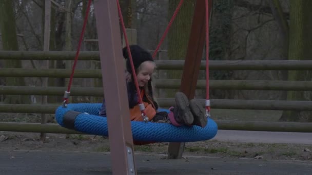 Bambino siede su un nido altalena padre sta spingendo sua figlia sta giocando su un altalena in un parco bambino e papà stanno ridendo famiglia hanno un resto su un parco giochi — Video Stock