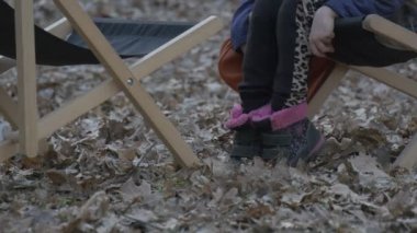 Sarışın kız bir masa sandalye üzerinde oturan ve salıncak bacaklar düşmüş yaprakları yere çocuk ile kahverengi çanta üzerinde Resting Park sonbahar akşam zaman bulutlu içinde olduğunu
