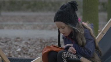 Kız bir güverte sandalyede oturan ve salıncak onu bacaklar çocuk Resting bir Park düşmüş yaprakları yere akşam zaman bulutlu gün Opole Polonya açık tarih içinde