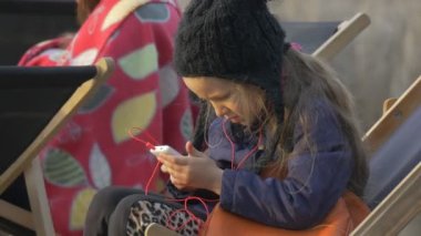 Her telefon ve dinleme müzik insanlar vardır oturma etrafında Her sarışın kız dinlenme Pier akşam zaman güneşli gün Opole Polonya açık havada üzerinde oynayan kız