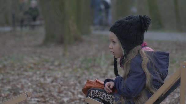 Blonďatá dívka sedí na lehátku a znuděný Kid je Klidový v Park padla listy na zem večer čas zataženo den Opole Polsko venku — Stock video