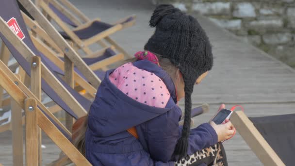 Fille assise sur la jetée au bord de l'eau et écouter de la musique Chaises de pont doublé dans une rangée Fille blonde reposant sur la jetée Soirée Heure Ensoleillé Jour Opole Pologne En plein air — Video