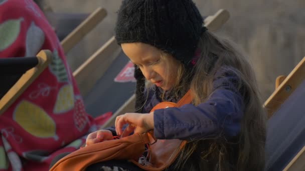 Flicka i solstol är skånska hörlurar tråd människor sitter runt hennes blond flicka vilar på piren kvällen tid soliga dag Opole Polen utomhus — Stockvideo