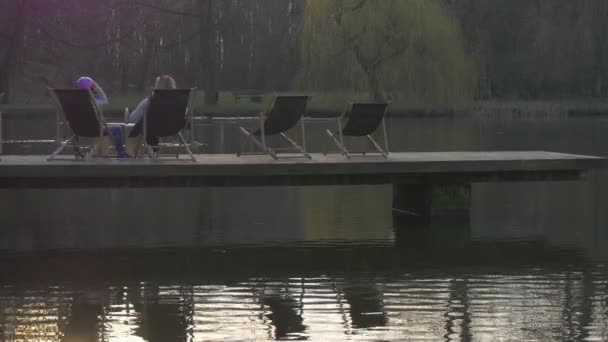人坐在躺椅上面平静的水面妇女搁在水面的码头表面晚上奥波莱波兰户外时间阳光灿烂的日子 — 图库视频影像