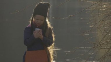 Küçük kız telefonunu çantadan bir yeşil göl kıyısında sakin sakin huzurlu gölet dalgalanma ağaç yeşil çim günbatımı bahar yürüme ayakta alır
