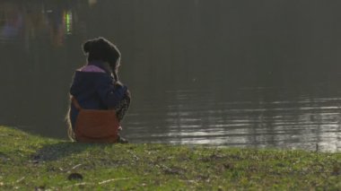 Küçük kız bir yeşil banka üzerinde bir göl yürüme yakınındaki sakin sakin huzurlu gölet Ripple su yeşil çim akşam alacakaranlık günbatımı Bahar üzerinde oturuyor