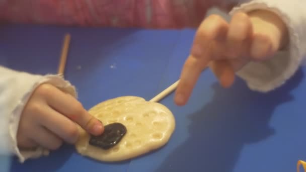 Маленькая девочка украшая карамель Внимательно учится делать конфеты карамель на палочке кондитера учит помогает нажать черный кусок декора — стоковое видео