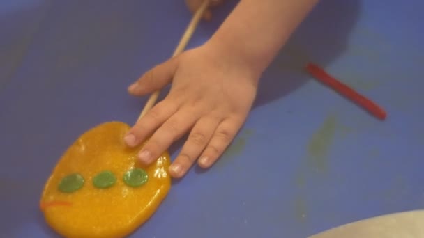 Mãos de criança Fixando uma decoração de caramelo para doces Aprendendo a fazer doces Caramelo circular amarelo em um confeiteiro de vara está ensinando as crianças como fazê-lo — Vídeo de Stock