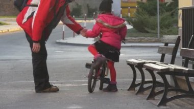 Baba bir bisiklet iter onu çalışan sırt çantası ile kırmızı ceketli baba adam Asfaltlı yol çocuk oturur akşam şehir sokak tarafından binmek için küçük bir kız yardımcı olur.