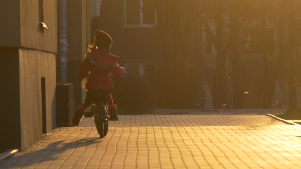 Dítě je na kole za roh domu v ulici večer Sunset dívčí siluetu v Sun Kid dlažební kameny se učí jezdit — Stock video
