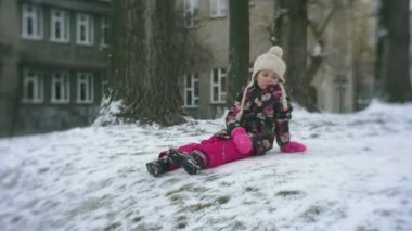 Küçük kız bir kar dönüm yavaş kış yetiştirme ve yürüyüş ayaz çiçekli ceket ve pembe pantolon zemin açık havada bahçede üzerinde oturuyor