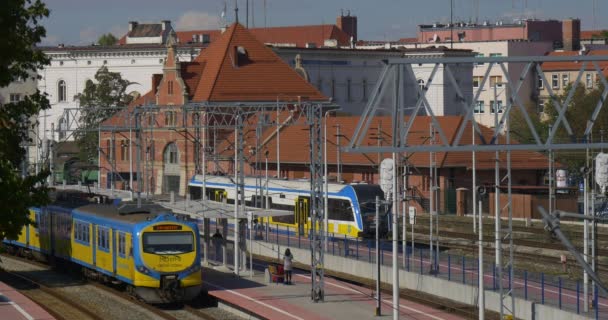 İnsanlar sırt çantası Platform adamla yürüyerek insanlar bekleyen mavi ve sarı yolcu elektrikli trenlerin tren istasyonunda bekliyoruz — Stok video