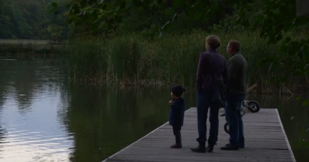 Man kvinna och barn lilla flicka familj står på trä Pier tittar på vatten grön vass träd är runt sjön Sky reflektion porlande vattnet — Stockvideo