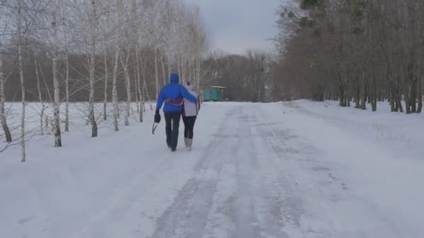 Bir erkek ve bir kadın kol kola yol adam boyunca mavi kış ve kadın beyaz kış ceket gri gökyüzü bulutlu kış günü açık havada yürümek — Stok video