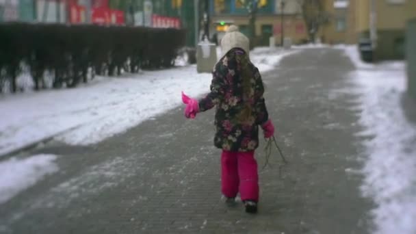 Kislány gyaloglás futás ugrás egy udvarban a téli lassított gazdaságban egy lapáttal és ágak fagyos hó lány virágos kabát Pink nadrág — Stock videók