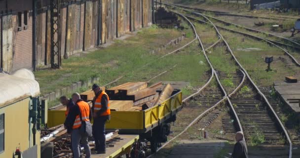 Arbeiter in orangefarbener Arbeitskleidung Arbeiter auf gelbem Lokomotivplateau mit Eisenbahnschwellen Zwei Arbeiter kommen zum Bahnhof — Stockvideo