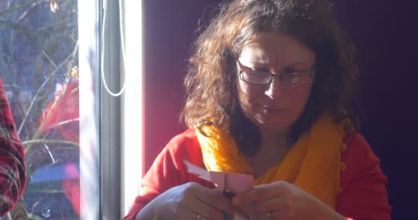 Woman in Glasses is Cutting a Pink Paper Cutting a Fir-Tree Out ajuda as crianças a fazer aplicações de inverno de um ano novo Mulher educadora ou mãe está sorrindo — Vídeo de Stock