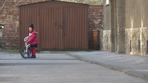 Отец учит свою дочь ездить на велосипеде, сидя рядом с велосипедом папа бежит к девушке Гараж Сити-стрит в солнечный день Спрингтайм — стоковое видео