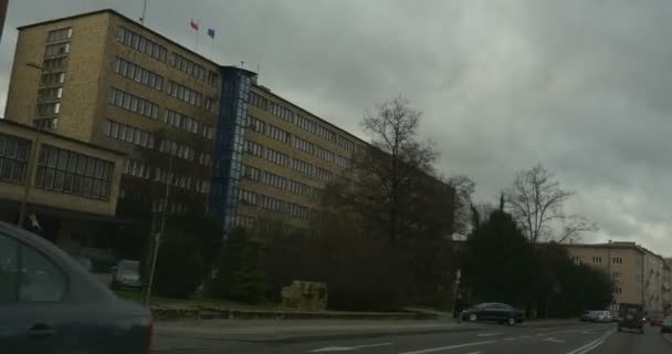 Antiguo coche de la torre con la cámara dentro de ella se mueve por la calle de la ciudad a lo largo de un edificio viejo que da vuelta y que conduce por un puente Otros coches en el día nublado de la carretera — Vídeo de stock