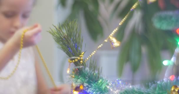 父に役立ちます飾るクリスマス ツリー松ゴールデン ビーズ女の子に女の子が立っていると彼女の手カラフルな憂の家族のお祝いを見てみる — ストック動画