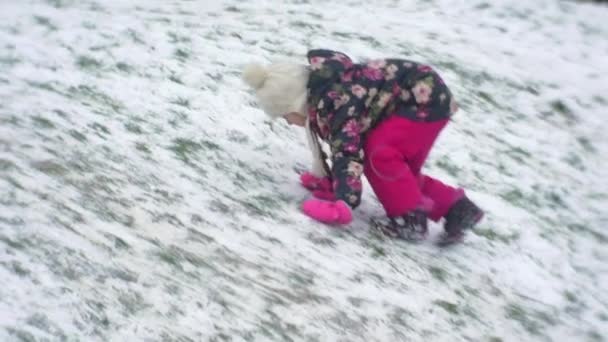 Little Girl met vlecht is klimmen op de heuvel voeten Slide door het verhogen van de sneeuw omhoog wandelen op een werf in Winter gebouw Frosty meisje in gebloemde jas handschoenen — Stockvideo