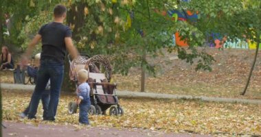 Oğulları Ile Man Baba Park'ta OynuyorLar Zemin den Kuru Yapraklar Kusma Bebek Pram İnsanlar Oyun Alanında Erkek Kadın ve Çocuklar Yürüyüş