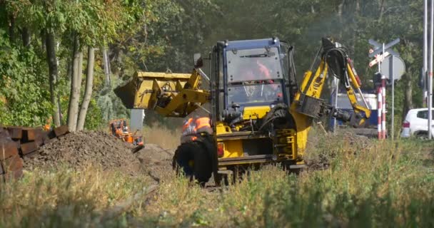 Рабочие копают жёлтый экскаватор выгружает земляное здание на лесной дороге Гроув на заднем плане Машины проезжают по дороге — стоковое видео