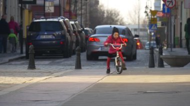 Çocuk at binme hızlı bisiklet şehir sokak Opole Polonya şehir gün kız kırmızı ceketli sürme arasında insanlar tarafından bir cadde Sunny gün bahar yürüyor