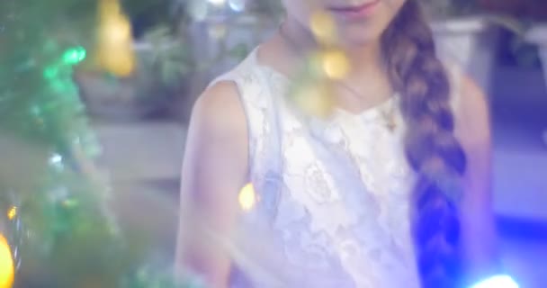 Lány gyaloglás körül egy fenyő új évet fa beszél Shying Golden Bell-koszorú a Korácsonyi, családi ünneplés lány, kék szemét — Stock videók