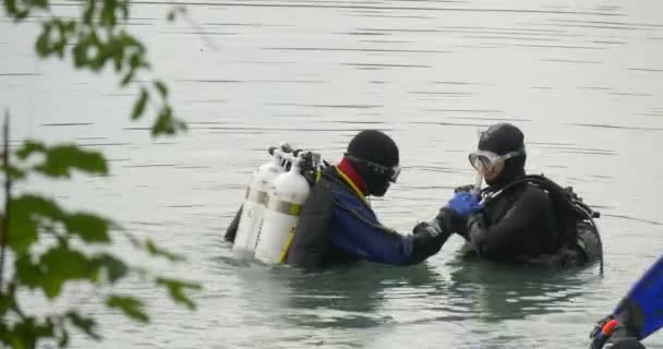 Двое мужчин ныряльщиков в купальниках стоят в воде, проверяя оборудование голубого Флиппера третьего водолаза. — стоковое видео