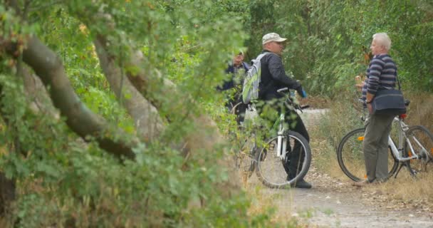 Двое мужчин стоят с велосипедами разговаривающих мужчин на велосипедах Мужчина и женщина появляется тропинка на Грин Хилл Парк лесных зеленых Buches падения зеленых деревьев — стоковое видео