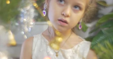 Violet küpe kız bir yeni yıl ağacı çam altın çan-Garland ve renkli Lamplights aile kutlama mavi boncuk çelenk koyarak