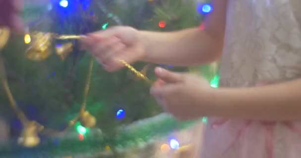Abuelo padre ayuda a la niña a poner una guirnalda de campanas de oro a un árbol de año nuevo pino coloridas luces están provocando brillante decoración celebración familiar — Vídeo de stock