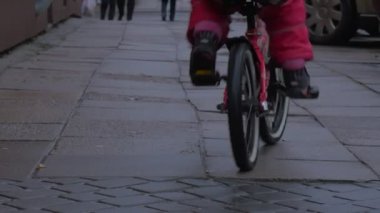 Çocuk parke fayans şehir Street boyunca bir kaldırım yürümek insanlar park etmiş arabalar Cityscape küçük kız tarafından çiçekli ceket açık havada bir bisiklet sürme