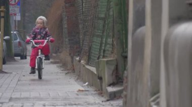 Çocuk at binme oynarken açık havada Bisiklet geri beceriksizce şehir sokak arabalar vardır park boyunca bir kaldırım yol işaretleri Cityscape, küçük bir kız çiçekli ceket olduğunu
