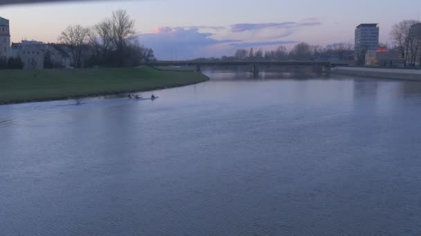 Sportler paddeln Kanu-Stadt am Flussufer Männer im Kajak gleiten über den Flussgrünen Park in der Nähe der Wasserautobrücke durch die bewölkte Abenddämmerung — Stockvideo