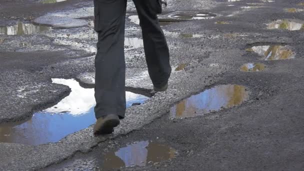 Mochilero en rojo está saltando a través de los charcos que corren por el camino húmedo Pies Primer plano Asfalto húmedo después de la lluvia Reflejo del cielo en un día soleado del agua en invierno Primavera — Vídeos de Stock