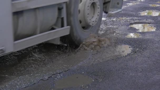 Camion avec cabine bleue est conduit par les flaques d'eau de la route humide dans un puits Roues de voiture Journée ensoleillée Réflexion du soleil dans une eau Asphalte humide Route non réparée En plein air — Video