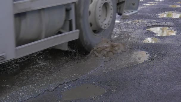 Nákladní automobil s modrými kabina je poháněn mokré silnici louže vody v jámy auto kola slunečný den slunce odraz v s vodou mokrý asfalt neopravené silniční venku — Stock video