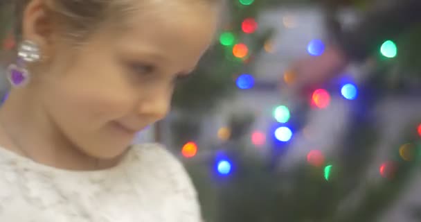 Menina em coroa e brincos com pedras violetas dançando no pinho de árvore de ano novo decorado com grânulos grinaldas ampliações coloridas avô pai — Vídeo de Stock