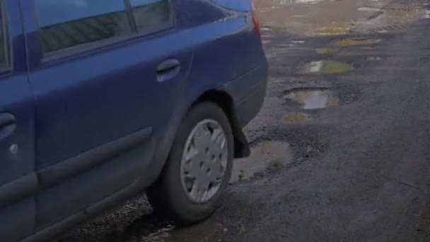 Mörkblå bil drivs av puddles Opole Polen City Day bilens hjul nummer på en stötfångare vatten i en pölar oreparerade väg himmel reflektion i ett vatten — Stockvideo