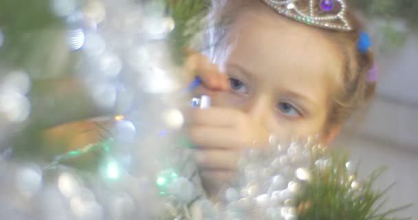 Chica está decorando un árbol de año nuevo con guirnaldas de cuentas azules poniendo una guirnalda al pino Golden Bell-Garland y coloridas luces Celebración familiar — Vídeos de Stock