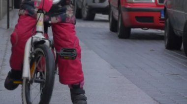 Çocuk oturur ve şehir sokak arabalar vardır park boyunca bir kaldırım yol işaretleri Cityscape küçük kız tarafından çiçekli ceketli bir bisiklet sürme olduğunu açık havada oyun