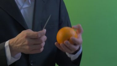 Adam gelir oturur ve beyaz gömlek bir yeşil ekran genç işadamı ve siyah takım elbise bir parmağındaki altın yüzük elinde bıçak ile bir portakal soyma