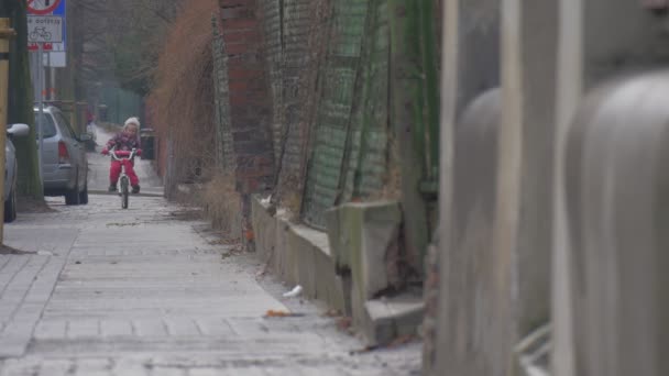 Enfant monte un vélo de retour par la ville Les voitures de rue sont garées le long d'un trottoir Panneaux routiers Paysage urbain Petite fille en veste fleurie joue à l'extérieur — Video