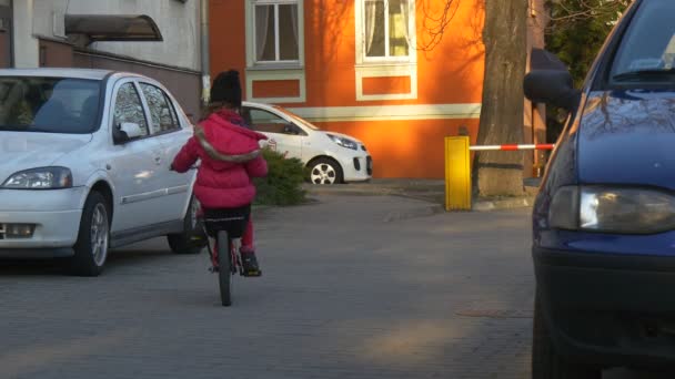 Liten flicka Rider en cykel av bilarna är parkerade bostads hus i Opole Polen barn är ridning bland bilar br gatan Sunny Day våren — Stockvideo